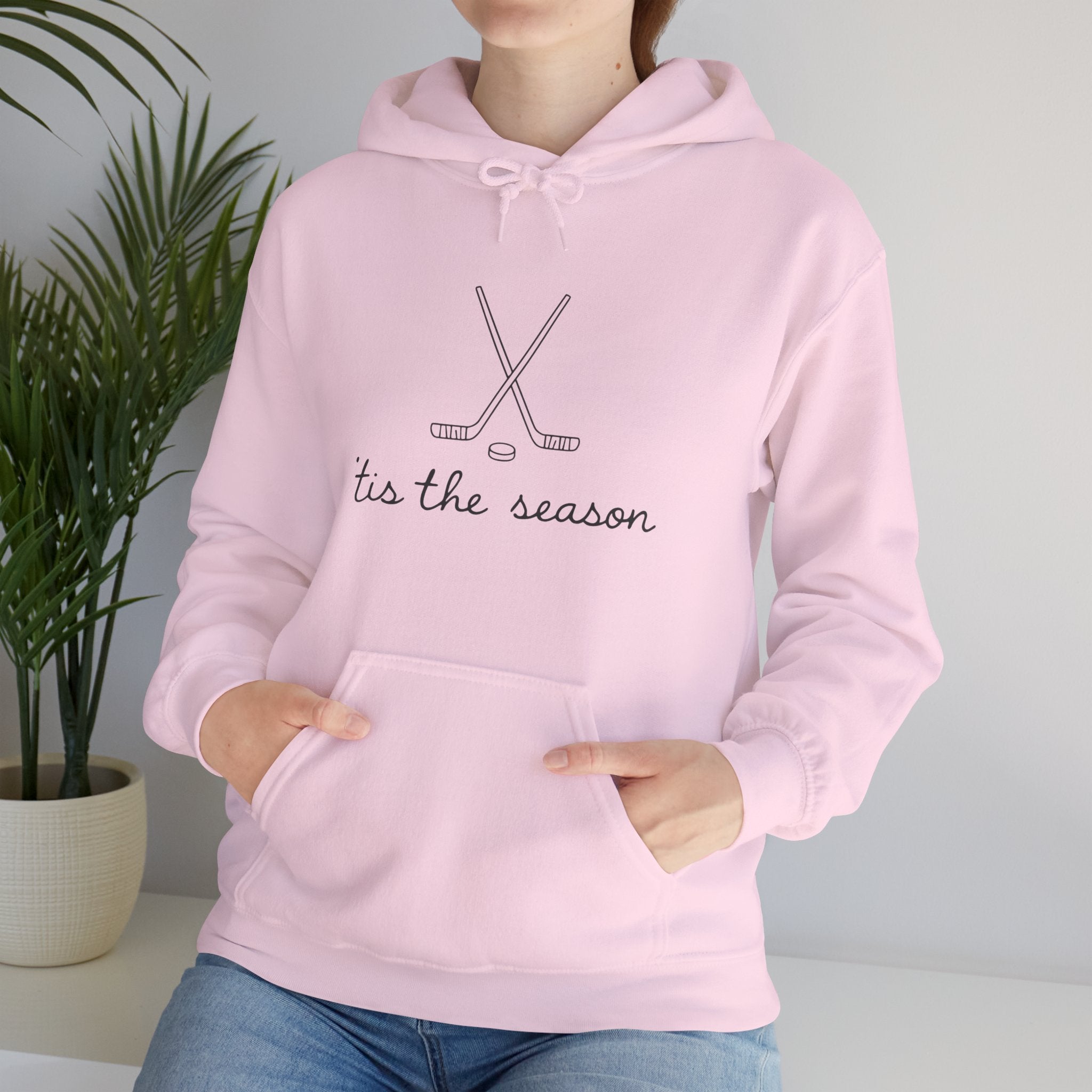 Person wearing a pink hoodie with 'tis the season text and hockey stick graphics.