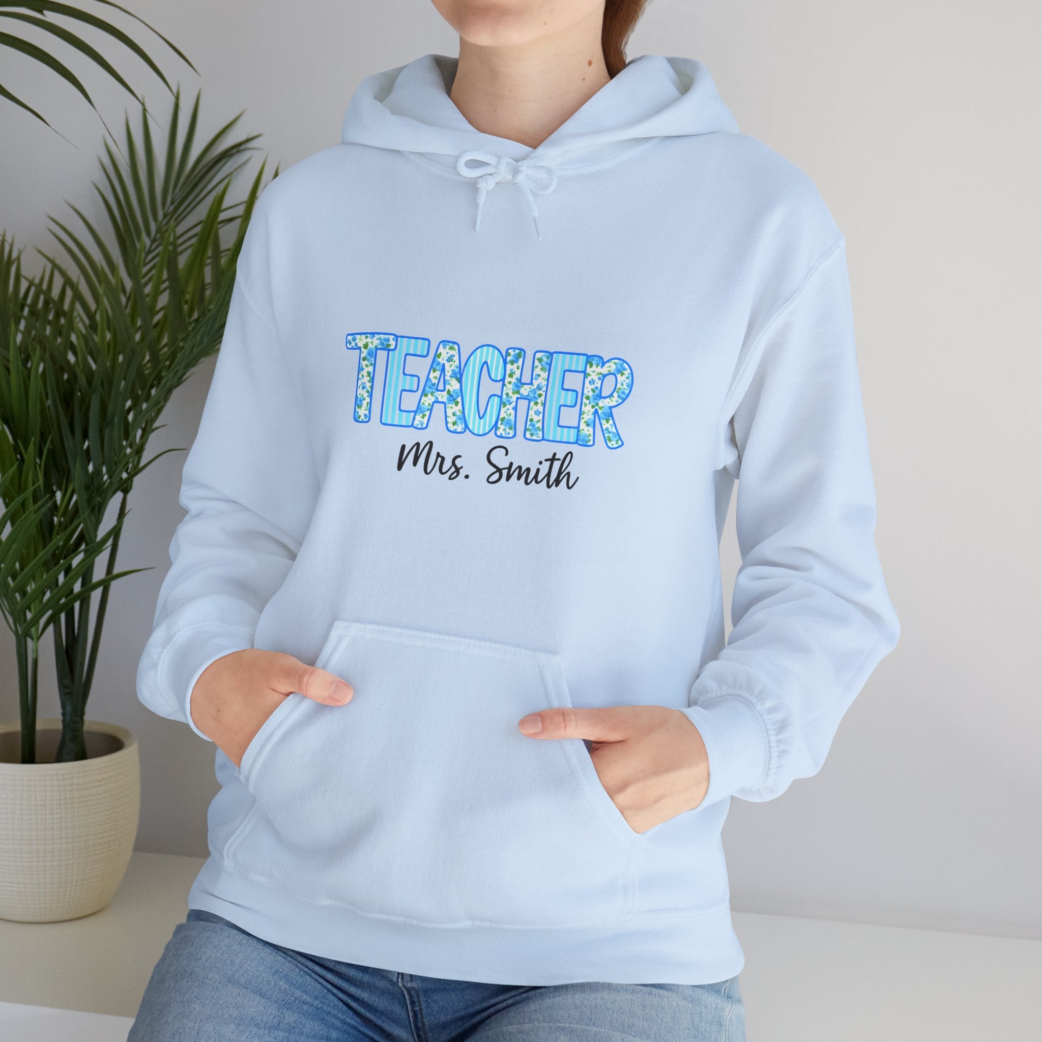 Light blue hoodie with 'TEACHER Mrs. Smith' text worn by a person, against a neutral background.